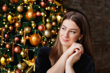 Altınla bir Noel ağacının arka planına bakan gülümseyen genç bir kadının portresi. Kadın rüyasında ellerini yüzüne kavuşturdu..