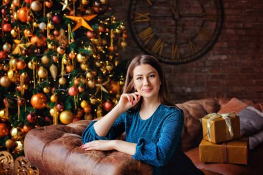 Düz saçlı ve makyajlı güzel bir esmerin portresi. Gece elbisesi giymiş güzel bir kız Noel ışıklarının arkasında poz veriyor. Mutlu Noeller.