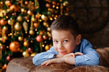 Çocuk güzel bir Noel ağacının yanında başını ellerinin üzerine koydu. Bir çelengin arka planında bir çocuğun portresi..
