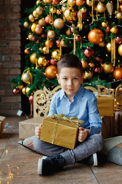 Uroczy Chłopiec Siedzi Pudełkiem Prezentów Pobliżu Choinki Złotymi Kulami Lampkami — Zdjęcie stockowe