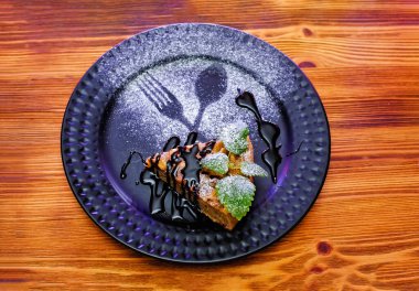 Bir parça ev yapımı kek, üzerine pudra şekeri serpiştirilmiş, ahşap bir masanın üzerinde.