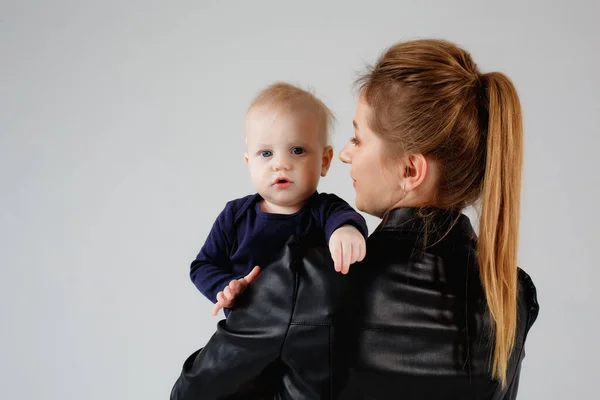 A mother in a black dress holds her son in her arms. A woman and a baby stand with their backs and hold the baby to the camera. Isolated on a gray background and space for text