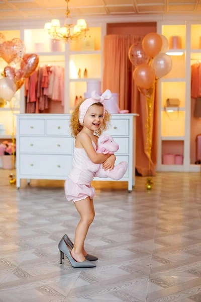 一个穿着粉色睡衣 手里拿着熊的小女孩试穿一双闪亮的高跟鞋 — 图库照片
