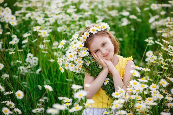 黄色のTシャツを着た女の子が 花束を手に 頭には花輪を手にデイジーの花を咲かせています 晴れた夏の日には何マイルもの畑 — ストック写真