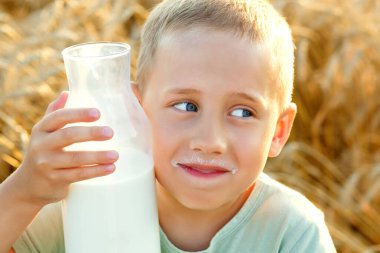 Buğday arka planında sütü olan bir çocuğun büyük portresi. Çocuk yüzüne cam bir şişe dayadı. Çavdar tarlasında gün batımında piknik.