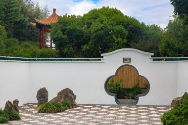Duvarında ay kapısı olan geleneksel bir Çin bahçesi, küçük bir pagoda ve dekoratif kaldırım.