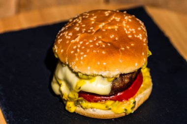 Siyah arka planda erimiş peynirli taze sığır etli çizburger.