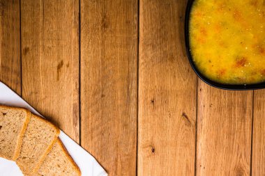 Bir kase çorba ve ahşap masada ekmek.