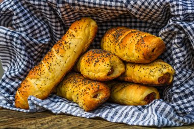 Hamurda pişmiş sosisler tuzlu ve haşhaş tohumlarıyla dolu kırsal bir sepetin içinde. Sosisli börekler, ev yapımı lezzetli hamur işleri..