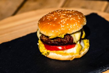 Siyah arka planda erimiş peynirli taze sığır etli çizburger.