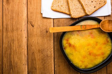 Bir kase çorba ve ahşap masada ekmek.