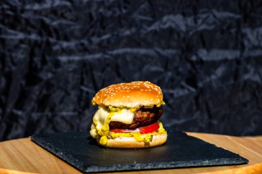 Siyah arka planda erimiş peynirli taze sığır etli çizburger.