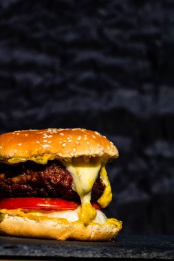 Siyah arka planda erimiş peynirli taze sığır etli çizburger.