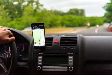 Araba gösterge panelindeki akıllı telefondaki waze haritaları uygulaması, sürücü, şehir trafiğinde doğru yolu göstermek için harita uygulaması kullanıyor. Bükreş, Romanya, 2020.
