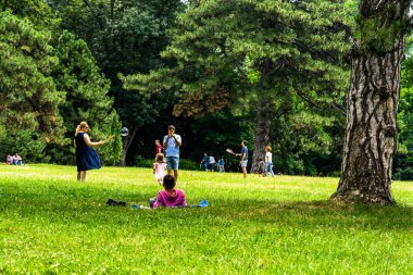 Annesi küçük kızı için sabun köpükleri yapıyor, insanlar piknik yapıyor ve parkta Coronavirus krizi sırasında eğleniyorlar ve Romanya 'nın Bükreş kentindeki Mogosoaia bölgesinin bahçeleri, 2020.