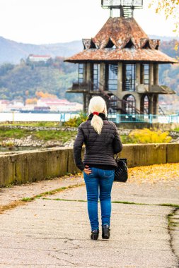 Sonbahar sokağında yalnız bir kadın yürüyor. Romanya 'nın Orsova kentindeki bir parkta sonbahar manzarası, turuncu yapraklar, 2020