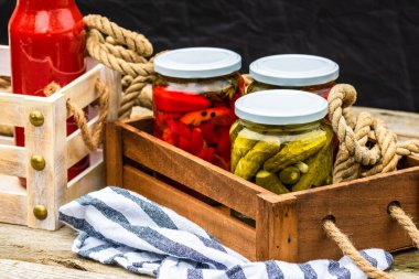Cam kavanozlu tahta sandık, kırmızı dolma biber turşusu ve salatalık turşusu. Çeşitli sebze turşulu kavanozlar. Kaba bir kompozisyonda yiyecek konseptini korudu.