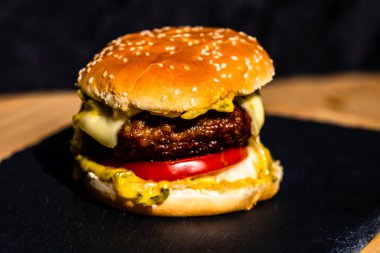 Siyah arka planda erimiş peynirli taze sığır etli çizburger.