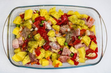 Çiğ sebzeler (patates, havuç, yeşil bezelye, kırmızı biber ve soğan) domuz eti sarımsağı ve pireks tepsisindeki baharatlar fırında pişirmek için hazırlanır..