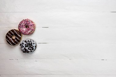 Beyaz ahşap masada renkli çörekler. Şekerli, şekerli, şekerli, şekerli, şekerli. Kopyalama alanı olan üst görünüm