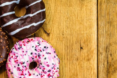 Ahşap masada renkli çörekler. Jöleli şekerli tatlı yiyecekler, çikolatalı donutlar. Kopyalama alanı olan üst görünüm