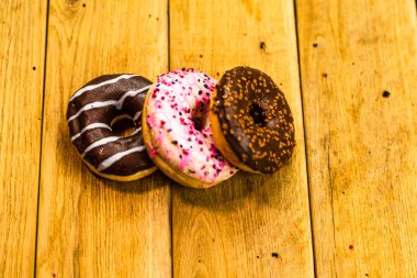 Ahşap masada renkli çörekler. Jöleli şekerli tatlı yiyecekler, çikolatalı donutlar. Kopyalama alanı olan üst görünüm