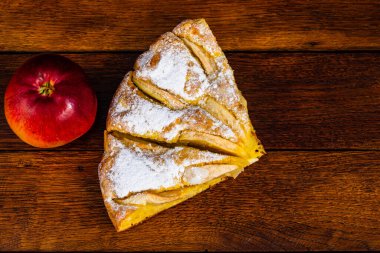 Tahta üzerinde şeker tozu ve kırmızı elmalı taze pişmiş elmalı turta dilimleri. Ev yapımı elmalı pasta..