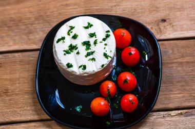 Kahvaltı, peynir ve kiraz domatesleri tabakta, ahşap ahşap tahta bir masa arkasında..