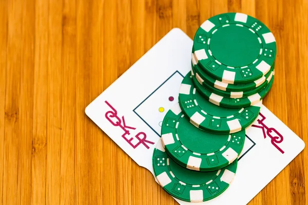 Playing cards joker card and poker chips close up, isolated on wooden table. Casino concept, risk, chance, good luck or gambling.