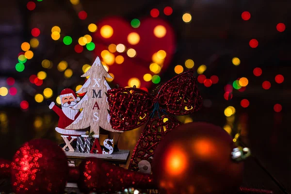 Arka planda bulanıklık ve odak ışıkları karşısında Noel süslemeleri. Noel Baba, ren geyiği, Noel ağacı ve ışıltılı Noel toplarıyla ahşap bir Noel kızağı çek.