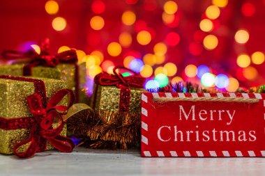 Mutlu Noel ahşap tabelası ve ışıltılı Noel hediyeleri. Bulanık ışık arkaplanındaki Noel kompozisyonu.