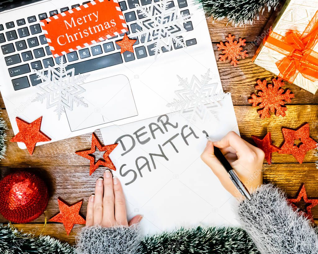 Writing Dear Santa for Christmas. Christmas letter. Holding letter for Santa. Christmas composition on wooden board with Christmas garlands and decorations.