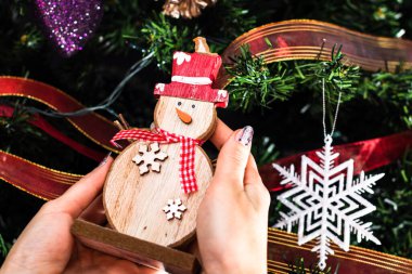 Noel ağacının önünde kardan adam heykelciği tutan eller. İzole edilmiş köknar ağacını süslemek