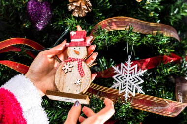 Noel ağacının önünde Noel süsü tutan eller. Noel süslemeleri ile köknar dallarını süslemek.