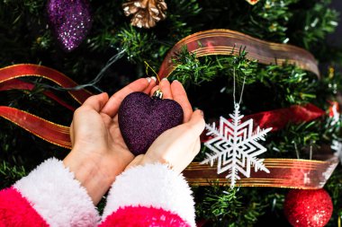 Noel ağacının önünde Noel süsü tutan eller. Noel süslemeleri ile köknar dallarını süslemek.