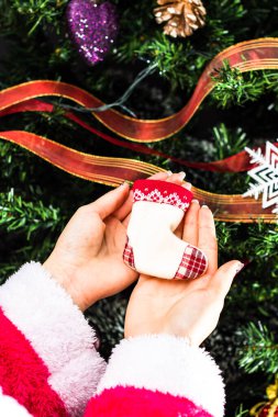 Noel ağacının önünde Noel süsü tutan eller. Noel süslemeleri ile köknar dallarını süslemek.