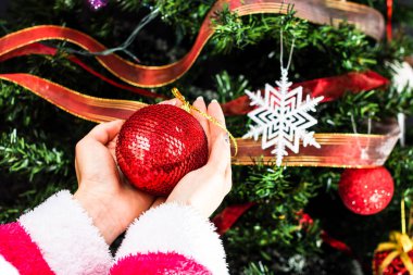 Noel ağacının önünde Noel süsü tutan eller. Noel süslemeleri ile köknar dallarını süslemek.