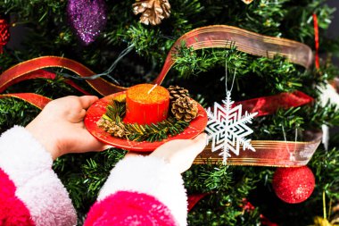 Noel ağacının önünde süslenmiş Noel mumunu tutan eller.