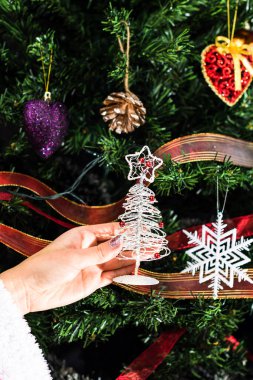 Hsnd Noel ağacının önünde küçük bir Noel ağacı heykeli tutuyor..