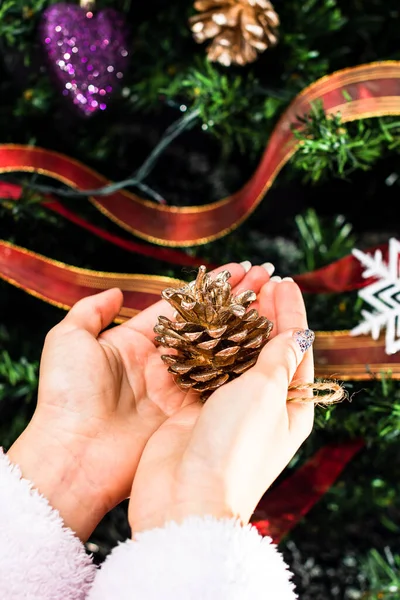 Noel ağacının önünde Noel süsü tutan eller. Noel süslemeleri ile köknar dallarını süslemek.