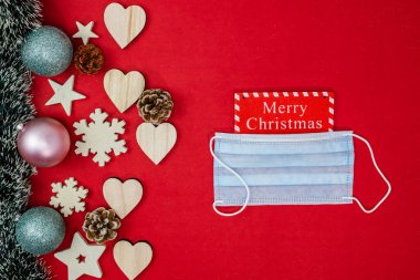 Noel kompozisyonunda cerrahi maske. Noel süsleri ve süslemelerle süslenmiş bir Noel arkaplanı. Kopyalama alanı olan üst görünüm.
