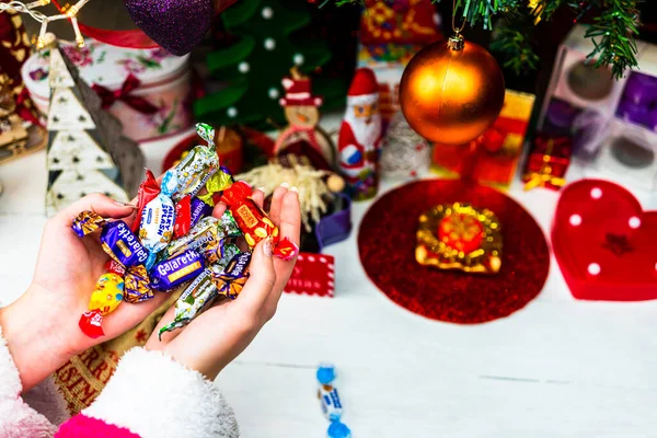 Noel ağacının önünde çikolatalı şekerlemeleri tutarken. Noel ağacı süslemek ya da hediyeleri açmak. Bükreş, Romanya, 2020