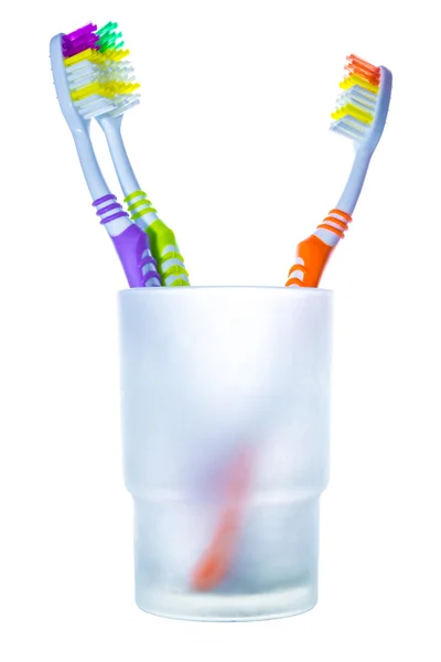 Three colorful toothbrushes in glass, two against one — Stock Photo, Image