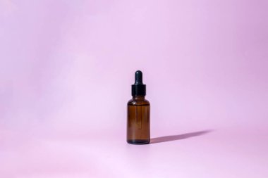 Pembe arka planda damlatan kahverengi cam şişe. Serum ya da gerekli yağ ambalajı. Kozmetik ürün Mockup.Boşluğu kopyala.