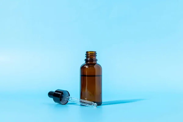 Glazen druppelflesje van bruin glas op een blauwe ondergrond werpt een schaduw. Vooraanzicht met kopieerruimte. Mockup van een cosmetisch product. Serum voor huidverzorging. — Stockfoto