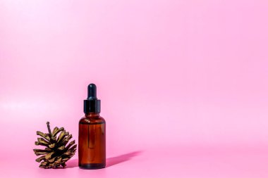 Pipetli kahverengi cam serum şişesi ve pembe arka planda, fotokopi alanı olan çam kozalağı. Vücut bakım serumu kozmetik cilt bakımı. Kopya alanı ile ön görünüm. Bir kozmetik ürünün maketi.