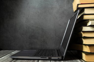 Kitap yığınının yanındaki masada açık bir dizüstü bilgisayar. Metnin için yer.