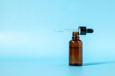 Mavi arka planda kahverengi cam damlatıcısı olan kozmetik şişesinin gölgesi var. Kopya alanı ile ön görünüm. Kozmetik ürününün bir kopyası. Cilt bakımı için serum.