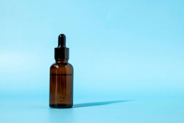 Mavi arka planda kahverengi cam damlatıcısı olan kozmetik şişesinin gölgesi var. Kopya alanı ile ön görünüm. Kozmetik ürününün bir kopyası. Cilt bakımı için serum.