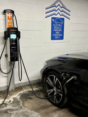 Otoparkın içindeki elektrikli araç şarj istasyonu, fişi takılı.